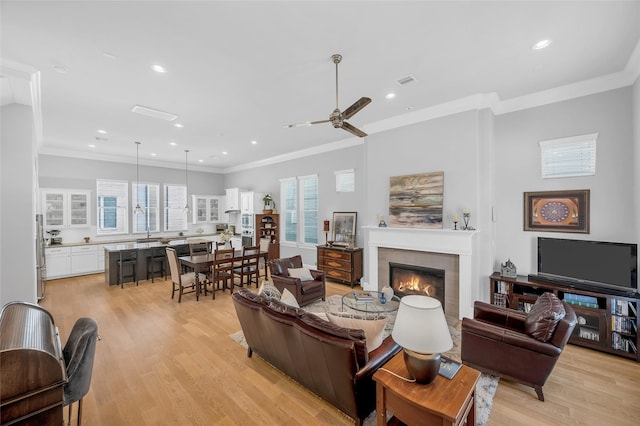 living room featuring crown molding, light wood-type flooring, a tile fireplace, and a ceiling fan
