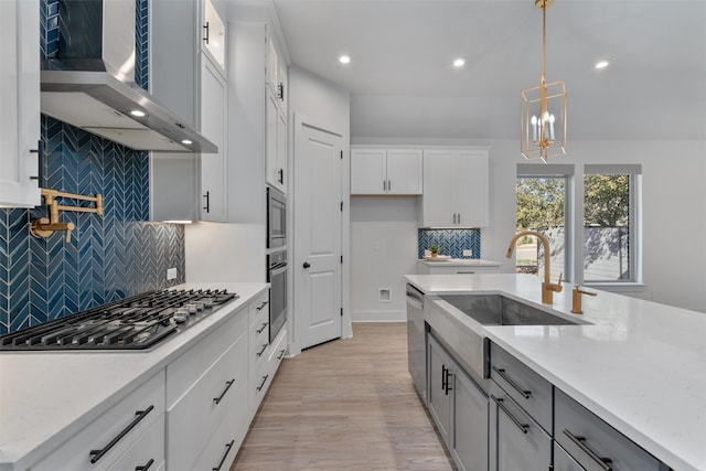 kitchen with white cabinets, decorative light fixtures, wall chimney exhaust hood, appliances with stainless steel finishes, and a sink