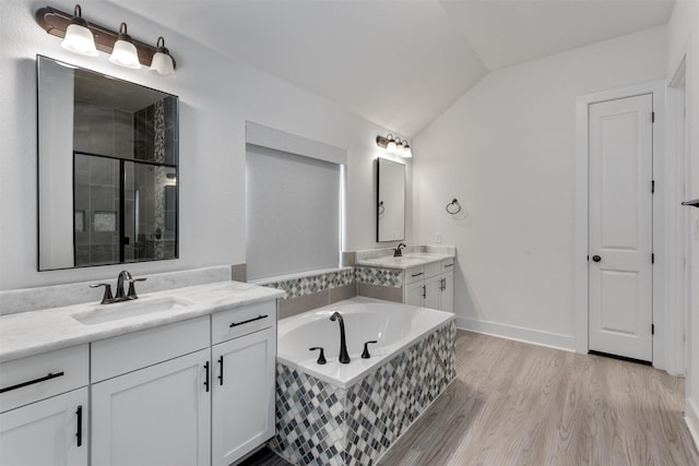bathroom featuring a garden tub, two vanities, a shower stall, a sink, and lofted ceiling