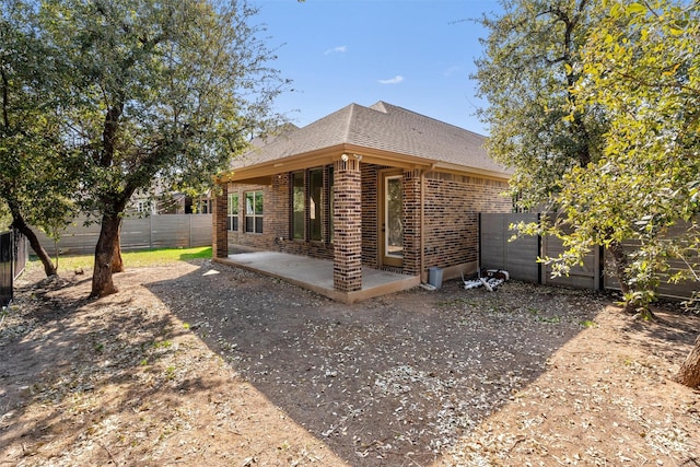 rear view of house with a patio, brick siding, a fenced backyard, and a shingled roof