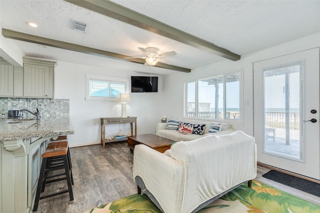 living area with beamed ceiling, ceiling fan, a textured ceiling, visible vents, and wood finished floors
