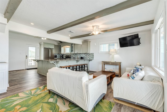 living room featuring beamed ceiling, ceiling fan, plenty of natural light, and wood finished floors