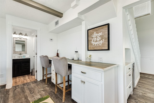 home office with dark wood-type flooring, visible vents, built in study area, wainscoting, and beam ceiling