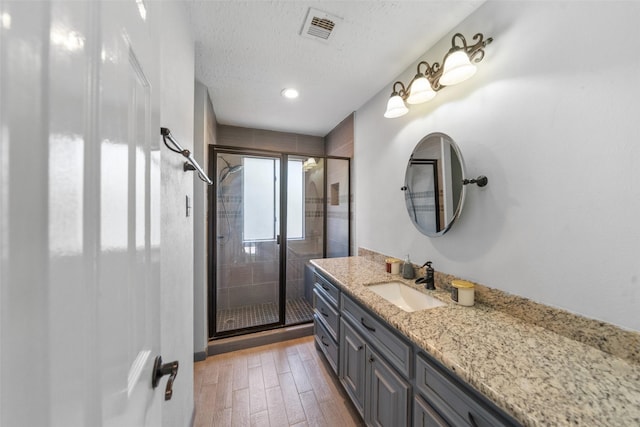 bathroom featuring a textured ceiling, visible vents, wood finished floors, a shower stall, and vanity