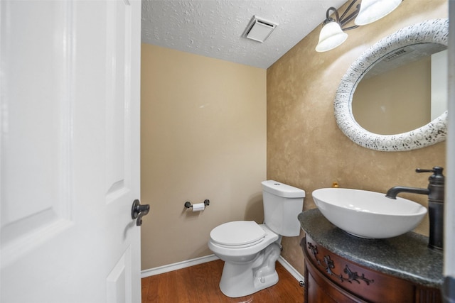 half bath featuring toilet, baseboards, visible vents, wood finished floors, and vanity