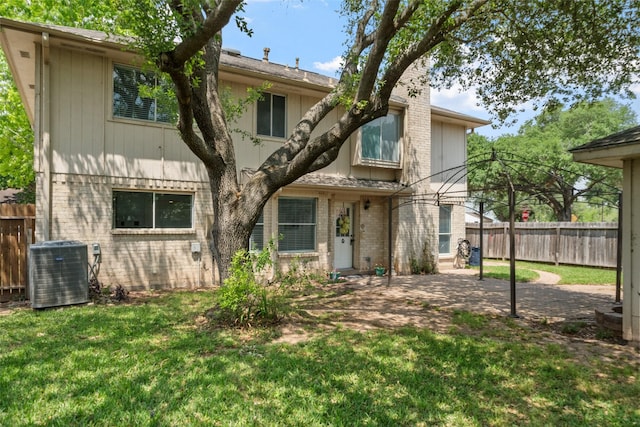 back of property featuring brick siding, a yard, central AC unit, and fence