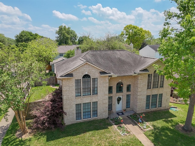 raised ranch featuring brick siding, roof with shingles, a front lawn, and fence