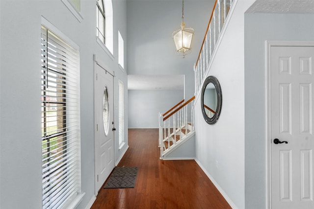 foyer featuring stairway, wood finished floors, a chandelier, a towering ceiling, and baseboards