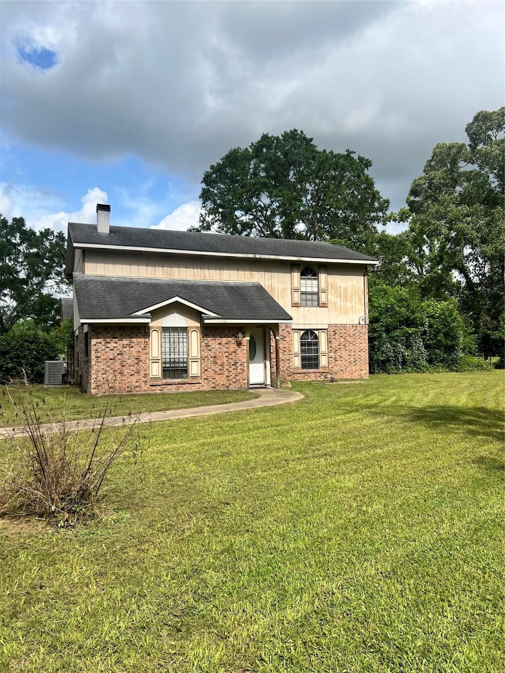view of front of house featuring cooling unit, brick siding, and a front yard