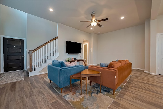 living room with wood finished floors, ceiling fan, baseboards, and stairs