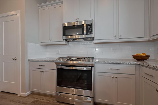 kitchen with appliances with stainless steel finishes, wood finished floors, backsplash, and light stone countertops