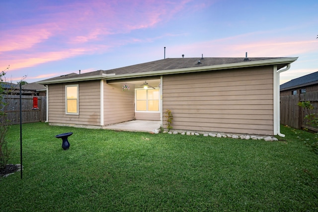 back of property at dusk with a yard, a patio, and a fenced backyard