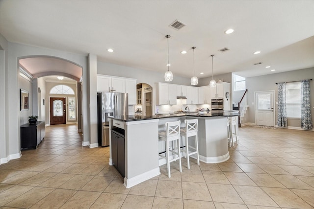 kitchen with visible vents, a healthy amount of sunlight, dark countertops, arched walkways, and stainless steel appliances