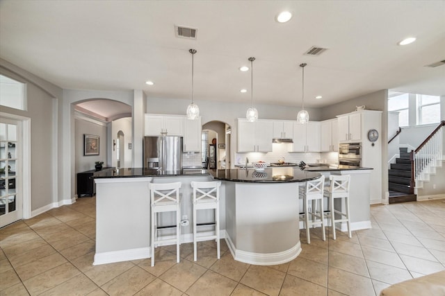 kitchen with decorative backsplash, dark countertops, arched walkways, light tile patterned floors, and stainless steel appliances
