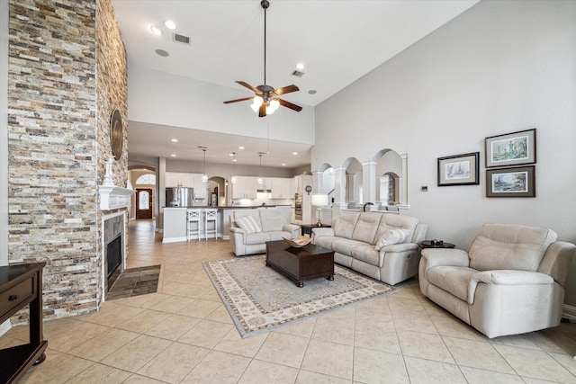 living room featuring ceiling fan, a fireplace, arched walkways, high vaulted ceiling, and light tile patterned floors
