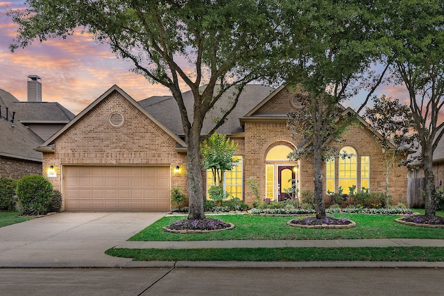 view of front of property with roof with shingles, an attached garage, brick siding, concrete driveway, and a lawn
