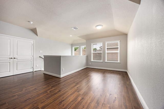 spare room featuring lofted ceiling, dark wood-type flooring, a textured ceiling, and visible vents
