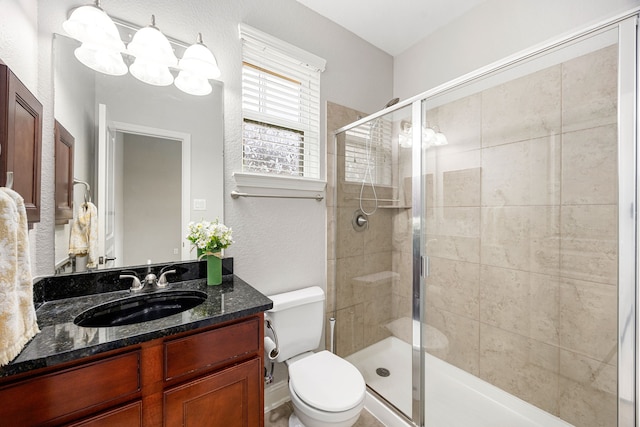 bathroom featuring a textured wall, vanity, toilet, a chandelier, and a stall shower