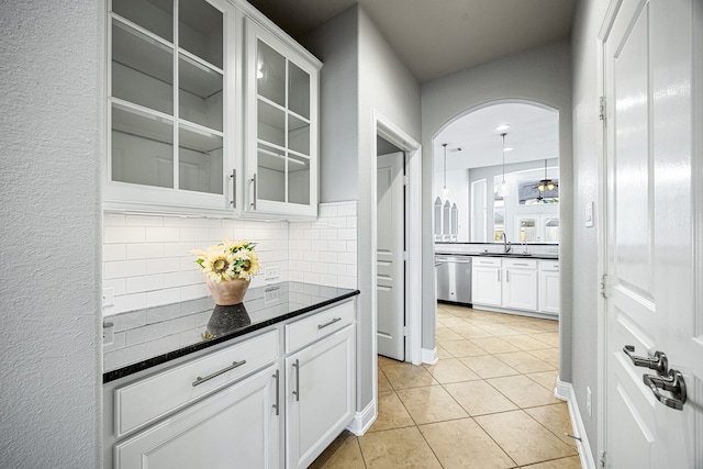 bar with stainless steel dishwasher, light tile patterned flooring, arched walkways, tasteful backsplash, and a sink