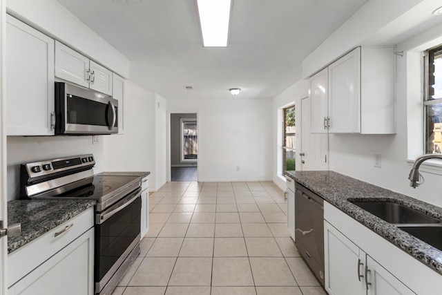 19822 Brightstone Dr, Humble, TX 77338 - kitchen with dark stone counters, light tile patterned floors, white cabinetry, appliances with stainless steel finishes, and a sink