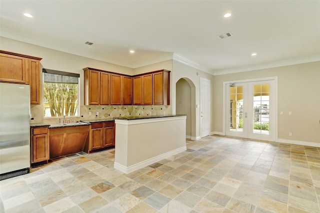 kitchen with brown cabinetry, visible vents, stainless steel fridge, arched walkways, and backsplash