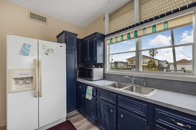 kitchen featuring a sink, blue cabinetry, white fridge with ice dispenser, visible vents, and light wood-style flooring