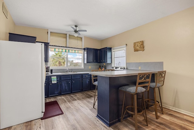 kitchen with blue cabinets, freestanding refrigerator, a breakfast bar, ceiling fan, and a sink