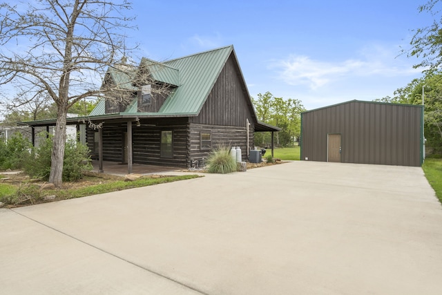 view of side of home featuring log siding, driveway, central AC, an outbuilding, and metal roof