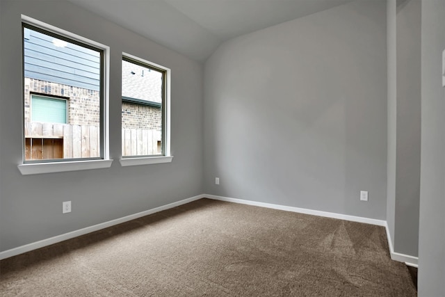 spare room featuring lofted ceiling, dark colored carpet, and baseboards