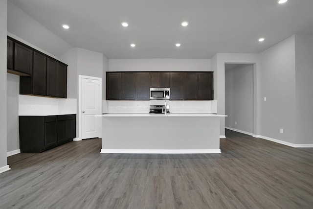 kitchen featuring tasteful backsplash, wood finished floors, a center island with sink, and stainless steel appliances