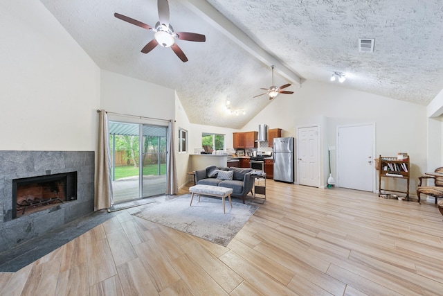 living room featuring visible vents, a tiled fireplace, light wood-type flooring, a ceiling fan, and a textured ceiling