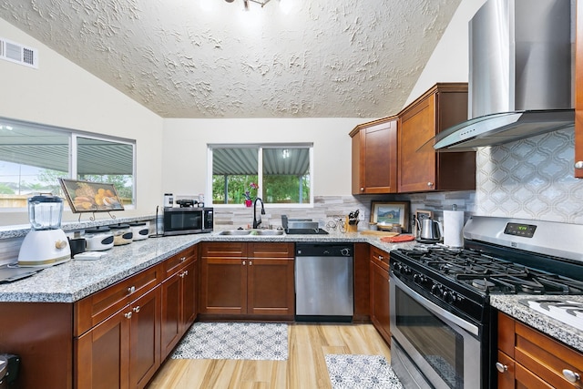 kitchen with wall chimney exhaust hood, light wood-type flooring, visible vents, a sink, and stainless steel appliances