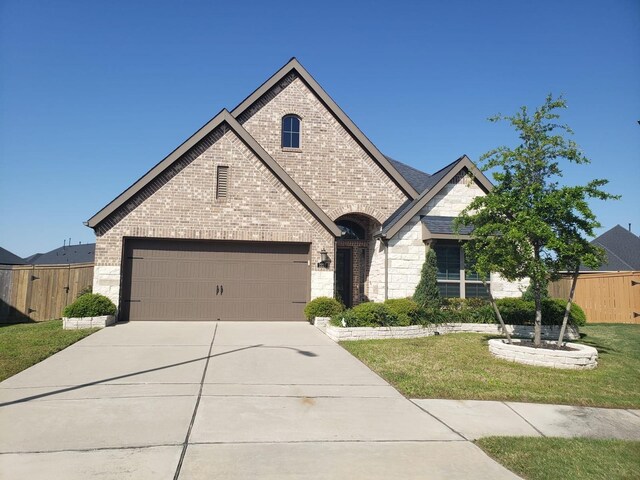 french provincial home with driveway, a front yard, brick siding, fence, and stone siding