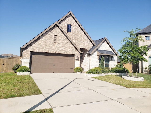 french country inspired facade with a front lawn, fence, stone siding, brick siding, and driveway
