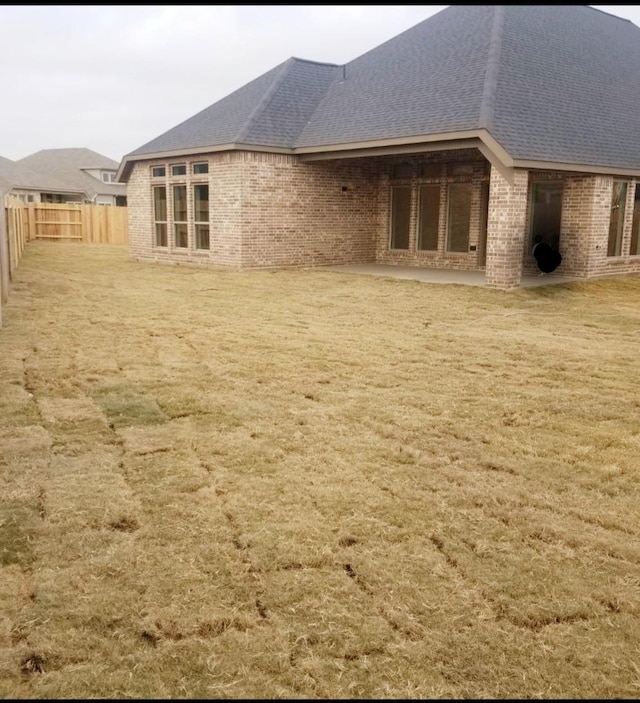 rear view of house featuring brick siding, fence, and a shingled roof