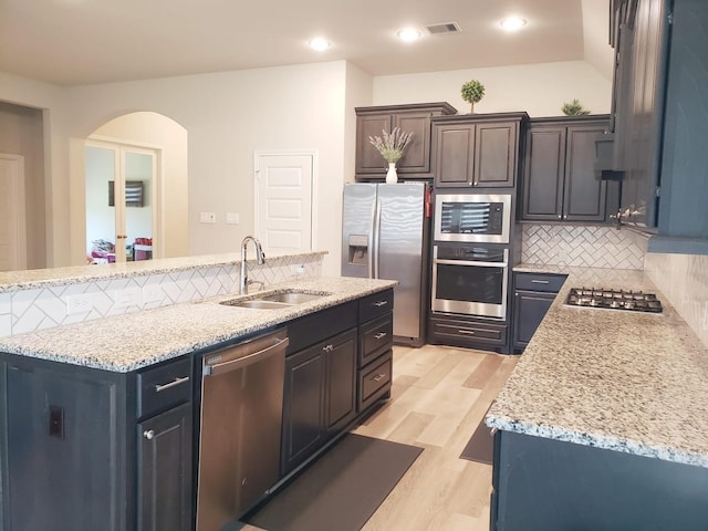 kitchen with decorative backsplash, appliances with stainless steel finishes, arched walkways, a sink, and light wood-style flooring