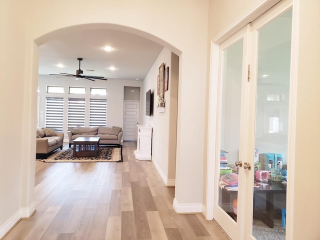 hallway with french doors, arched walkways, and light wood finished floors