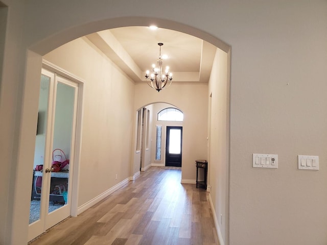 entryway with an inviting chandelier, a raised ceiling, arched walkways, baseboards, and wood finished floors
