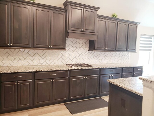 kitchen featuring light stone countertops, dark brown cabinetry, stainless steel gas stovetop, and tasteful backsplash