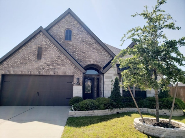 french country inspired facade with a garage, a front yard, driveway, and brick siding