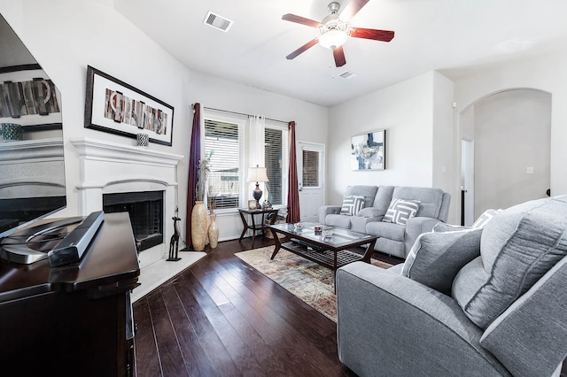 living room featuring visible vents, a ceiling fan, a fireplace with raised hearth, hardwood / wood-style flooring, and arched walkways