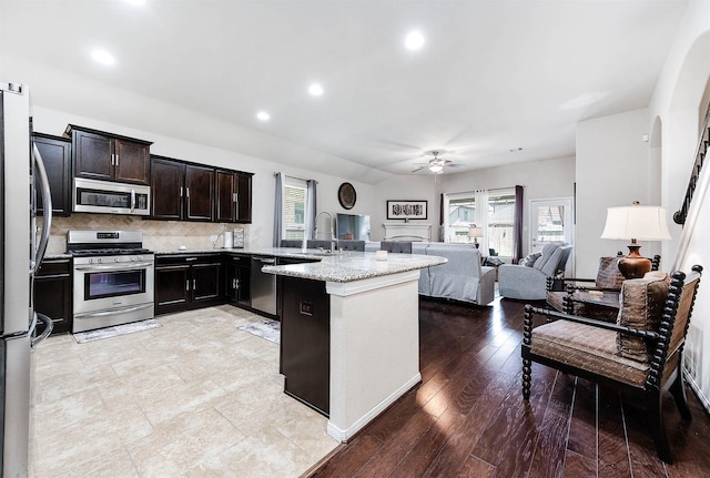 kitchen with decorative backsplash, a ceiling fan, a sink, open floor plan, and stainless steel appliances