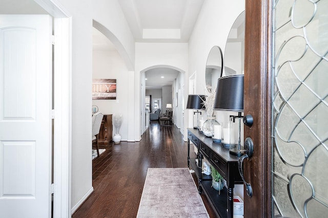 foyer with baseboards, arched walkways, and dark wood-style flooring