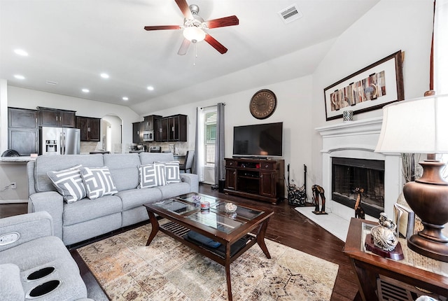 living area featuring ceiling fan, arched walkways, vaulted ceiling, visible vents, and dark wood-style floors