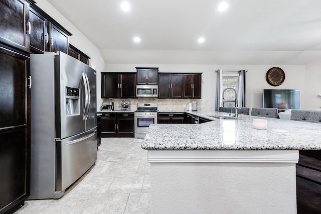 kitchen with recessed lighting, light stone counters, a sink, appliances with stainless steel finishes, and backsplash