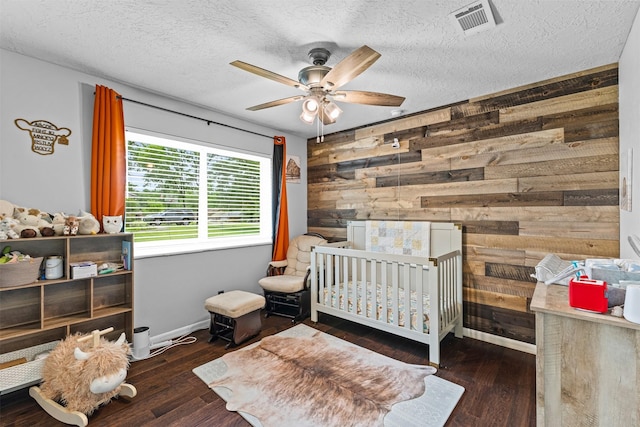 bedroom featuring a crib, wood walls, baseboards, wood finished floors, and visible vents