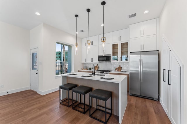 kitchen featuring dark wood-style flooring, visible vents, a breakfast bar area, decorative backsplash, and stainless steel appliances