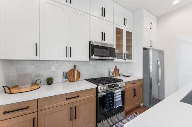 kitchen featuring backsplash, glass insert cabinets, light countertops, stainless steel appliances, and dark wood-style floors