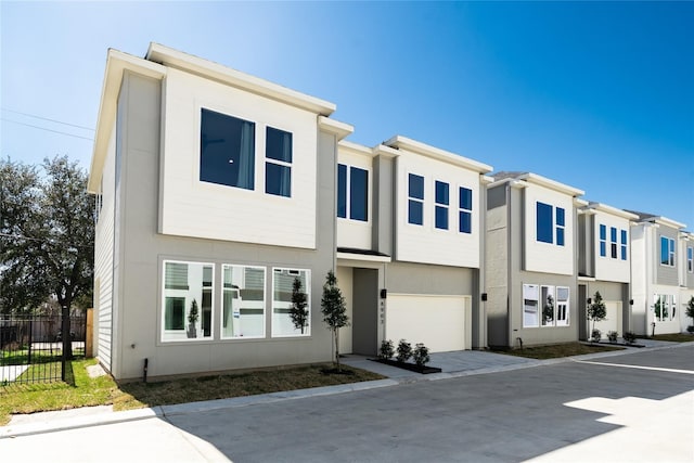view of property featuring concrete driveway, a garage, stucco siding, and fence