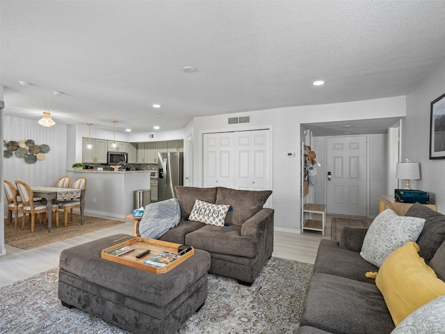 living room featuring light wood-style floors, recessed lighting, a textured ceiling, and visible vents